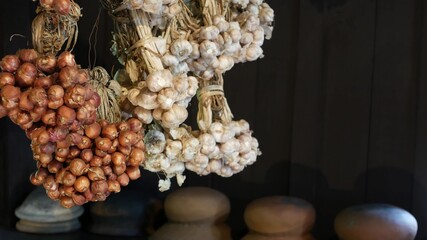 Dried onion and garlic in kitchen. Bunches of small dried onion and garlic hanging against dark wooden wall in kitchen.