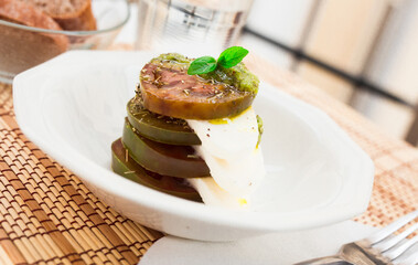 caprese salad with mozzarella, black tomatoes and pesto in white plate