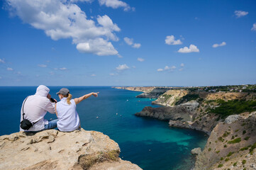 man and woman sitting together on mountain looking at beautiful nature on sea resort at summer or autumn