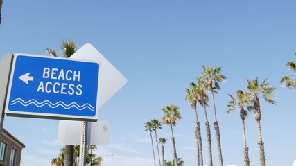 Beach sign and palms in sunny California, USA. Palm trees and seaside signpost. Oceanside pacific tourist resort aesthetic. Symbol of travel holidays and summertime vacations. Beachfront promenade