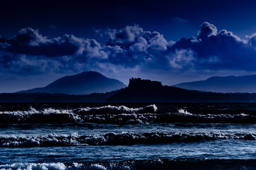 Island of Procida, Campania region, Italy. Image of the island with a castle silhouette seen from a beach with nocturnal and dreamy atmosphere and mood.