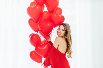 beautiful woman with heart shaped balloons standing ath the window and looking at the camera.