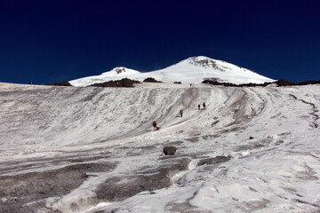 Climbing Elbrus. Snow-capped mountain peaks and figures of climbers in the foreground. Mountains covered with snow.