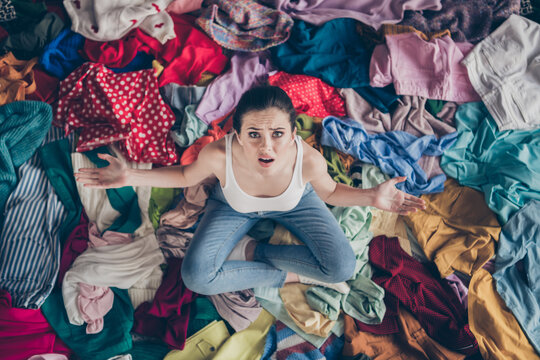 High Angle Above View Photo Of Stressed Helpless Lady Stay Home Spring Cleaning Household Sit Many Clothes Stack Floor Pick Select Outfit Nothing To Wear Concept All Stuff Dirty Indoors