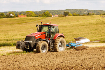 Obraz premium Farmer in a big red tractor preparing land with plow for sowing
