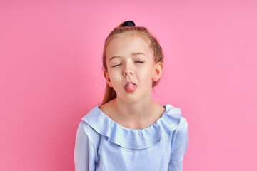 emotional crazy girl shows tongue at camera, beautiful child have fun alone, isolated on pink background