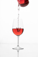 Red wine pouring into glass  on glossy white background with reflection.