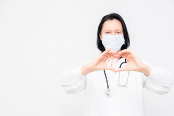 Woman doctor in medical mask shows heart symbol on white background with copy space