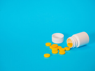 Yellow pills and plastic white bottle. Blue background with copy space for text. Healthy and medicine. Pain management. Drug abuse in teenage concept