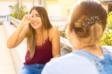 Two girls speaking in sign language in a public space. Deaf friends or couple communicating, having fun, pleasant conversation, sitting together