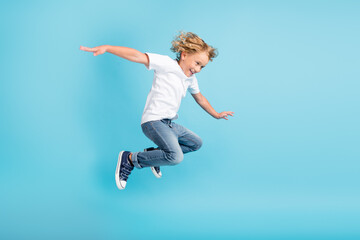 Profile photo of young boy jump fly movement hands wear white shirt jeans sneakers isolated blue...