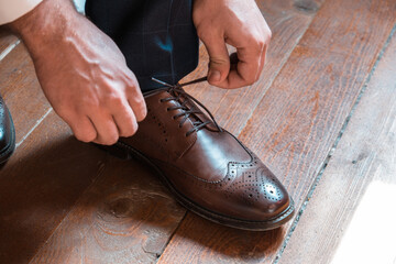 Close up view of man tying up brown shoes. Groom wearing elegant shoes on wedding day. 