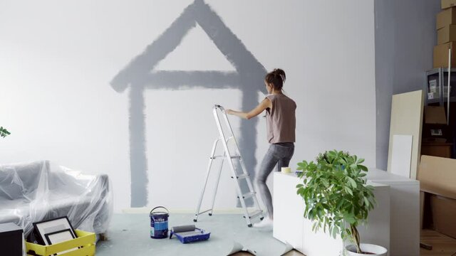 Young woman painting having fun while painting walls in apartment