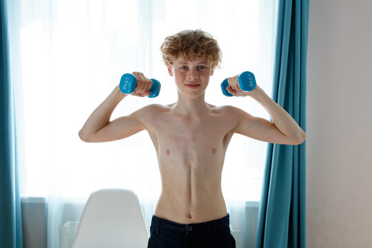 shirtless young caucasian strong teenager boy exercising at home, hold dumbbells in hands, pumping arm muscles. sport concept