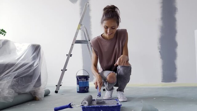 Happy woman painting wall at home using roller brush