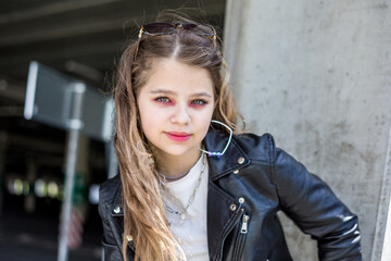 young schoolgirl with bright pink makeup in black leather jacket posing in the parking lot