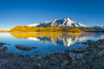 Paine mountain range in warm early morning light. The mountains reflect in the still and clear water of a small lake