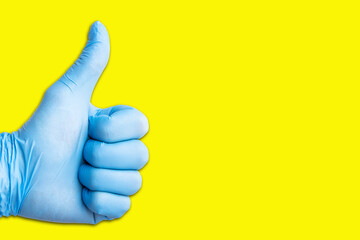 Hand in blue latex glove isolated on yellow with thumb up. Approval sign background.