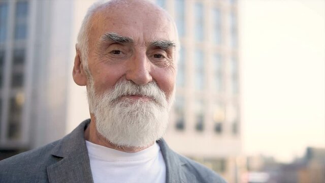 Portrait of mature gray bearded man looking at camera and smiling, outdoor