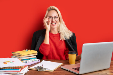 adorable caucasian woman love work in office, she is enjoying work with laptop, smile. isolated red background