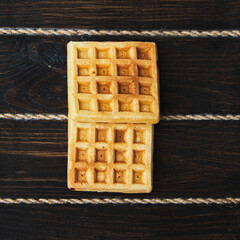 Two belgian waffles on dark wooden background. From top view