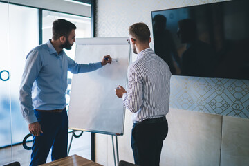 Back view of male colleagues in smart casual wear discussing ideas and share sketches for design in...