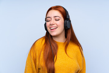 Redhead teenager girl over isolated blue background listening music