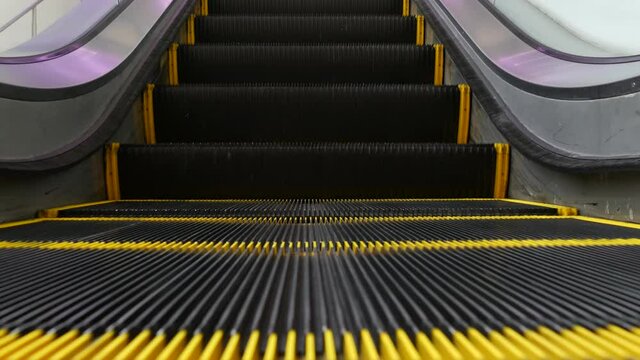 Low angle looped perspective view of modern escalator stairs. Automated elevator mechanism. Yellow line on stairway illuminated with purple light. Futuristic empty machinery staircase moving straight.
