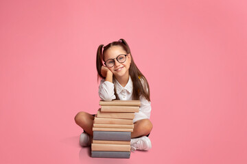 Start learning concept. Little girl in glasses and uniform, sits near stack of books