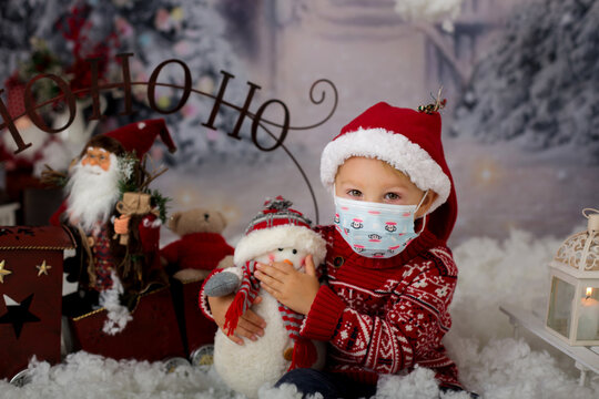 Cute boy, toddler child, having his christmas pictures taken playing in the snow outdoors, wearing protective mask