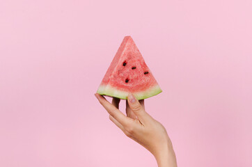 Hand holding slice of watermelon on pink background