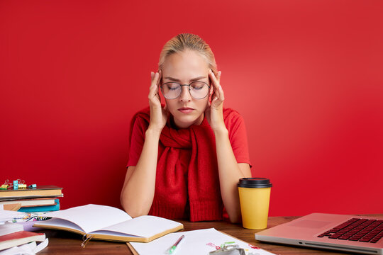 overworked unhappy and frustrated young caucasian woman in stress sitting at office desk, she has a lot of tasks in work, deadline, isolated red background