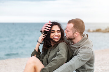 Young couple being sweet and romantic sitting at the beach. Millennial Girlfriend and Boyfriend together at an outdoors photoshoot. People enjoying the beach