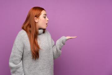 Redhead teenager girl over isolated purple background holding copyspace imaginary on the palm