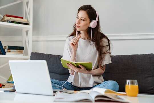Image of girl writing down notes while using laptop and headphones