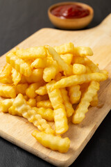 Tasty french fries with ketchup on cutting board, on the black table background