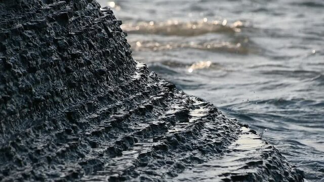 A flysch cliff in Moon Bay, Slovenia that often collapses and is dangerous to humans. Close up view of waves hit sedimentary rock layers. Low angle, slow motion, static shot, shallow depth of field
