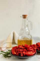 Homemade sun-Dried tomatoes, olive oil in a glass bottle, fresh rosemary and spices on a light background. Print for the kitchen. selective focus.