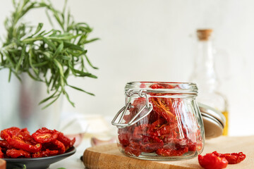 Homemade sun-Dried tomatoes, olive oil in a glass bottle, fresh rosemary and spices on a light background. Print for the kitchen. selective focus.