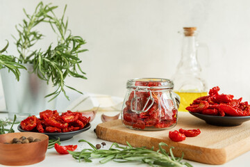 Homemade sun-Dried tomatoes, olive oil in a glass bottle, fresh rosemary and spices on a light background. Print for the kitchen. selective focus.