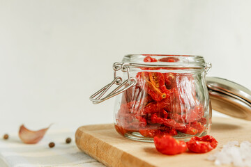 Homemade sun-dried tomatoes in a glass jar, garlic cloves, on a light background. place to copy. selective focus.