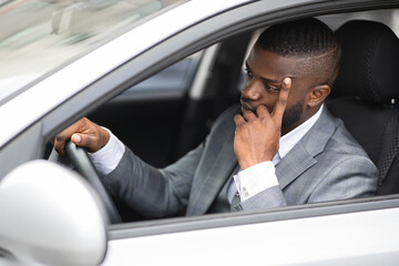 Pensive african businessman leaning on his hand while driving car