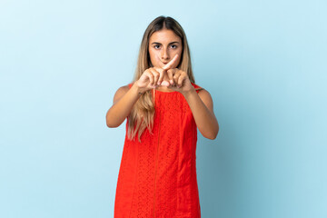 Young hispanic woman over isolated blue background making stop gesture with her hand to stop an act