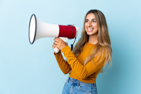 Young hispanic woman over isolated blue background shouting through a megaphone to announce something