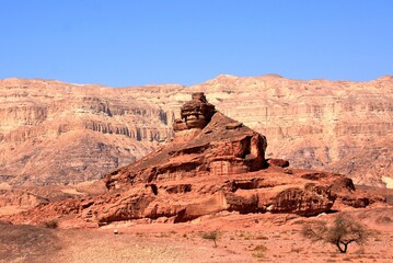 View on the arid mountain in triangle shape in Timna Park located in Negev desert in Israel. View is from side window of the car passing dirty asphalt road covered with sand and small dry stones.