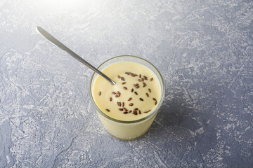 Glass of yellow mango or banana yogurt or smoothie with flax seeds on gray background. Turmeric Lassie (lassi). Healthy dairy snack. Copy space for text