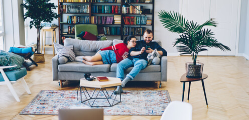 Cheerful couple in love browsing smartphones in living room