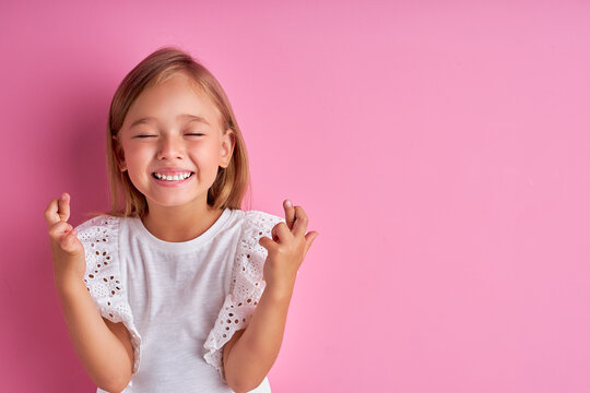 cheerful emotional girl keep fingers together, smile, shine with happines, dream. isolated pink background
