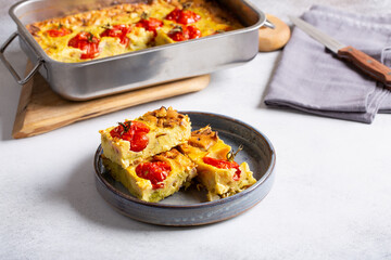 Vegetable clafoutis on gray plate on concrete background, savory pie with cabbage and whole cherry tomatoes. Vegetarian cuisine.
