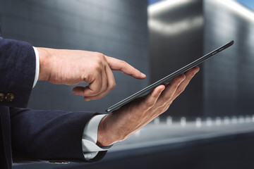 Businessman hand clicks on the screen of a digital tablet near the exterior of the business center at night, close up. Internet Work Concept